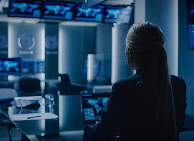 Woman at a computer in a control room with multiple screens in the background