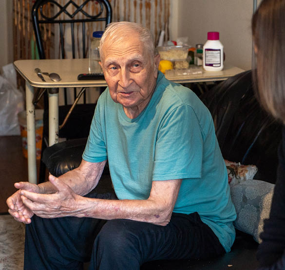 Older man sitting on a couch, talking with a visitor