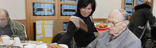 Woman serving food to an older man at a table