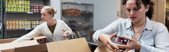 Two people packing food items into boxes in a pantry