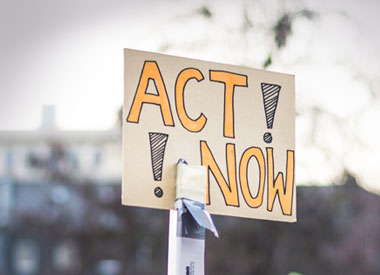 Handheld sign reading ‘Act Now!’